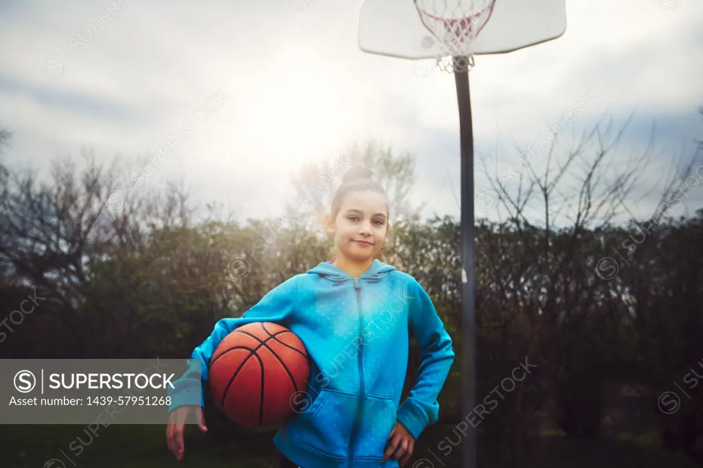 Young girl poised to play basketball under a sunny sky