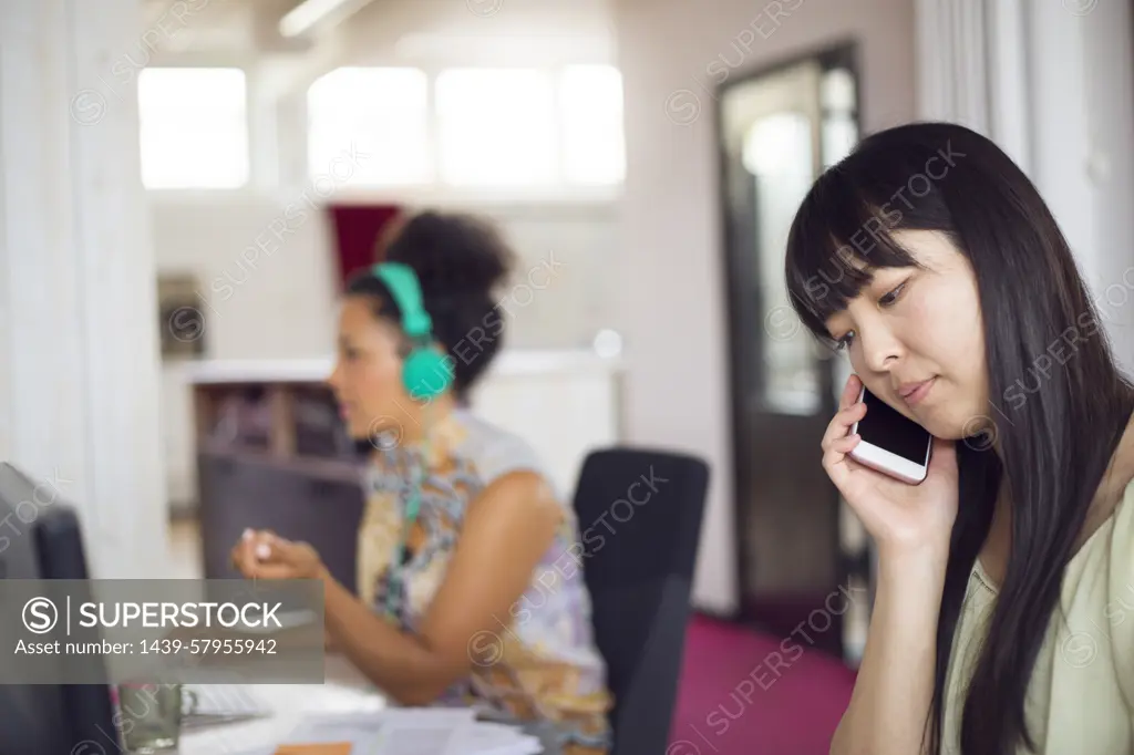 Two women working in an office environment, one talking on the phone and the other focused on her computer monitor.