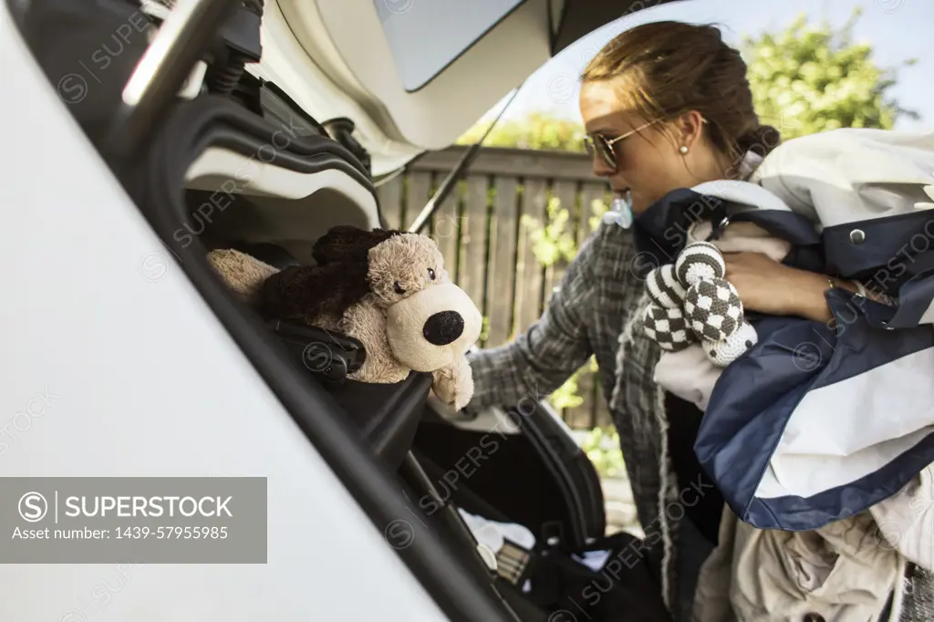 Busy mom packing the car with a stuffed toy and baby essentials.