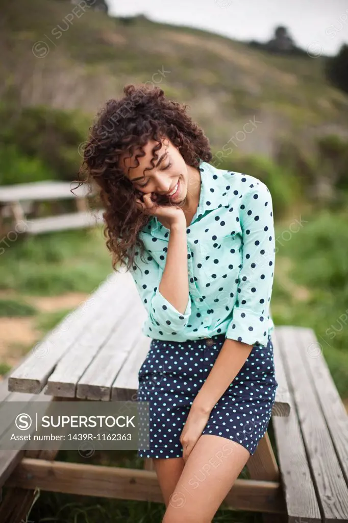 Young woman with hand in hair standing by picnic table, smiling