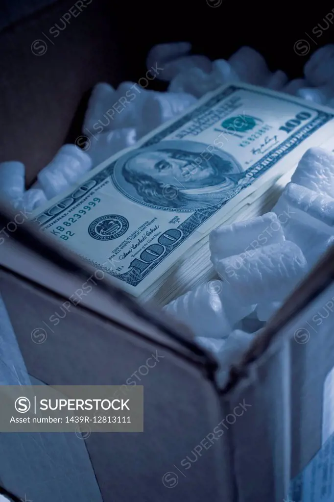 Stack of one hundred dollar bill in cardboard box with foam packing peanuts