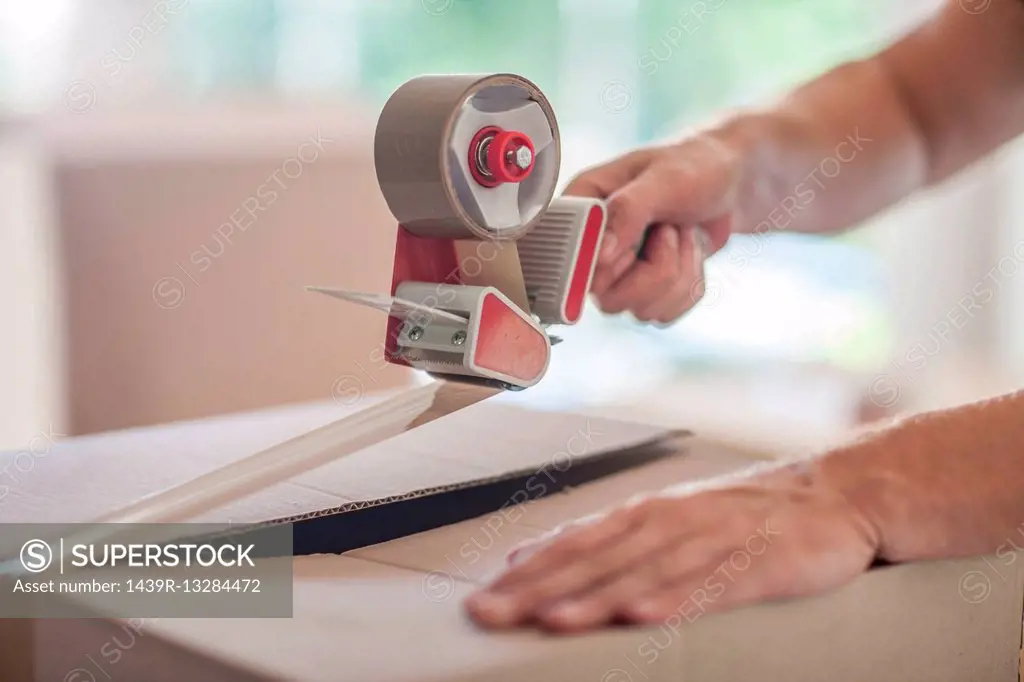 Man taping up box using tape dispenser, close-up