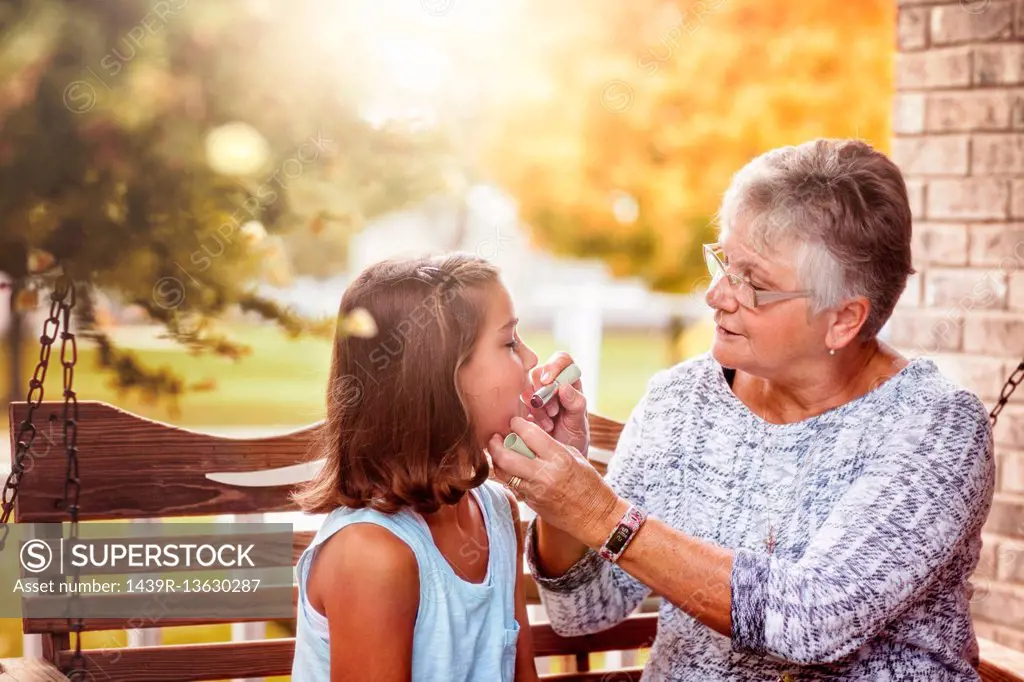 Grandmother and granddaughter sitting on porch swing, grandmother showing granddaughter how to apply lipstick