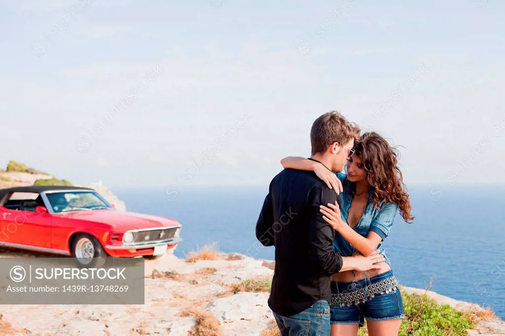 couple standing at cliff in front of car