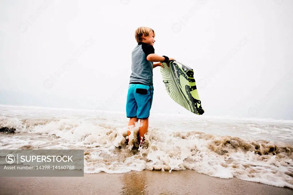 Young boy standing in sea, holding bodyboard