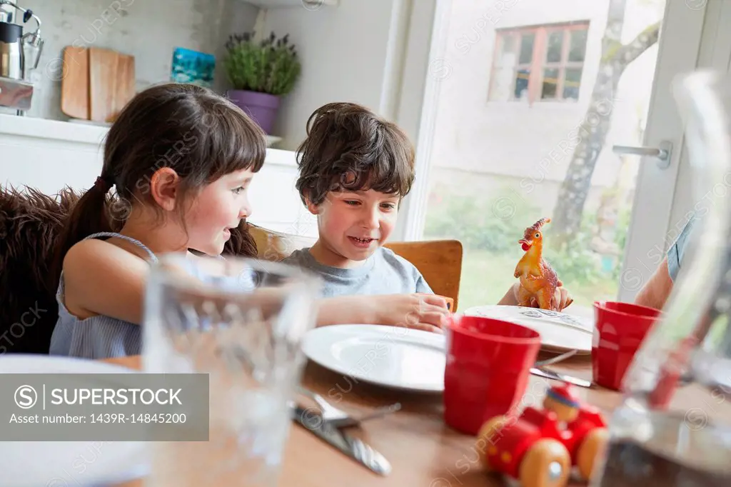 Young boy and girl sitting at dinner table, smiling