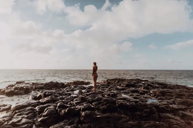 Swimmer standing on rocks by sea, Princeville, Hawaii, US