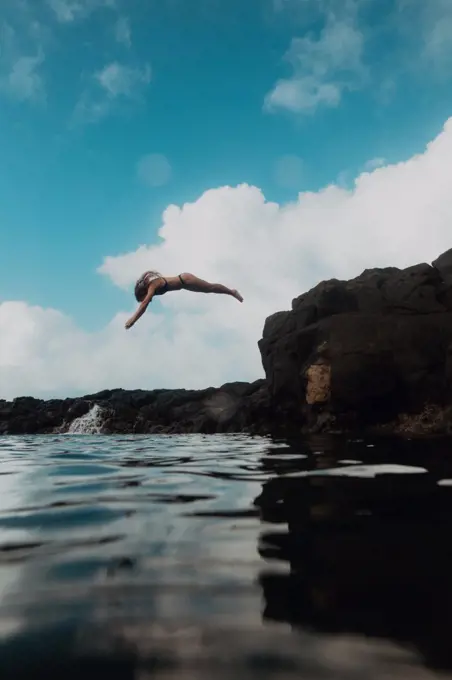 Swimmer diving off rocks into sea, Princeville, Hawaii, US