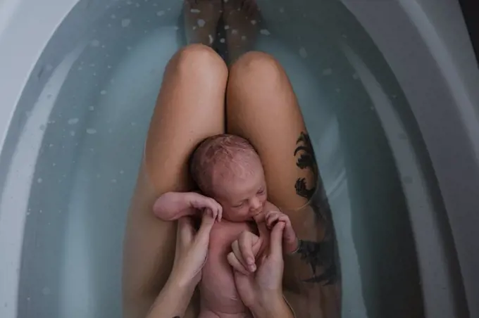 Mother with baby son on her lap in bath, cropped overhead view