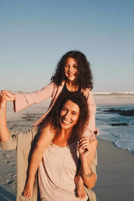 Mother giving daughter piggyback ride on beach