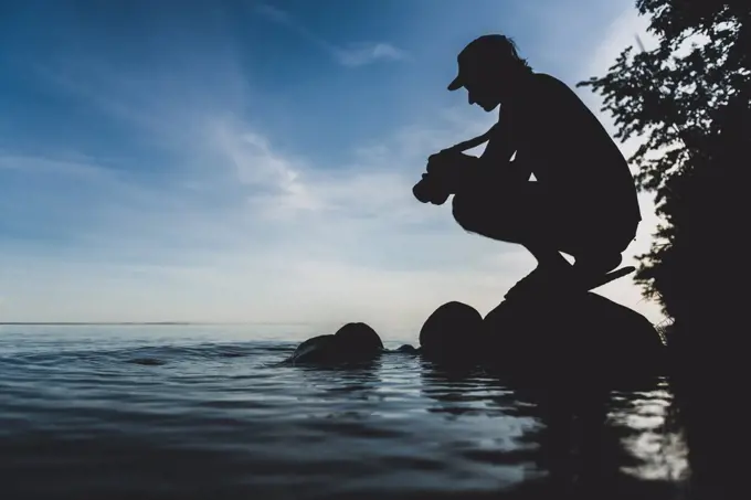 Silhouette of man crouching by the shore of a lake