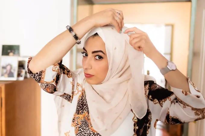 Young muslim woman putting on hijab headscarf