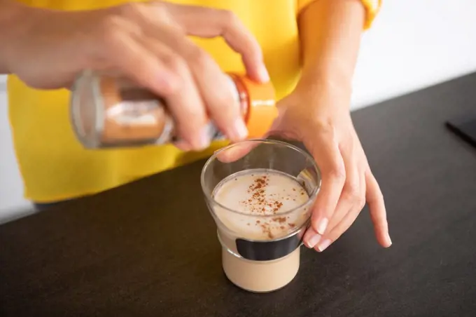 Portugal, Lisbon, Close-up of woman's hands sprinkling coffee with cinnamon