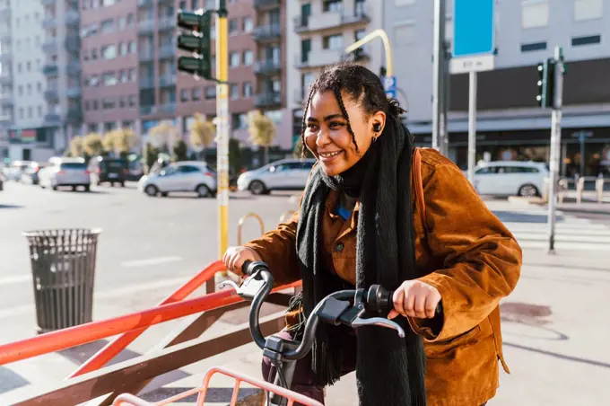 Smiling young woman with bicycle on city street