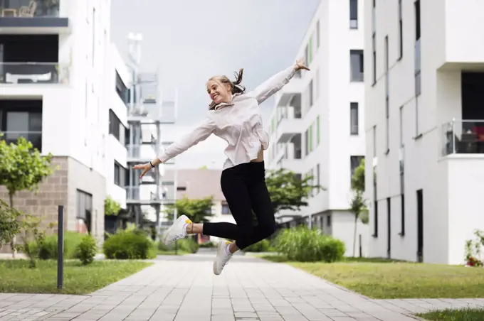 Smiling young woman jumping in modern neighborhood