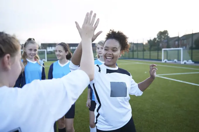 UK, Female soccer team members giving high five in field