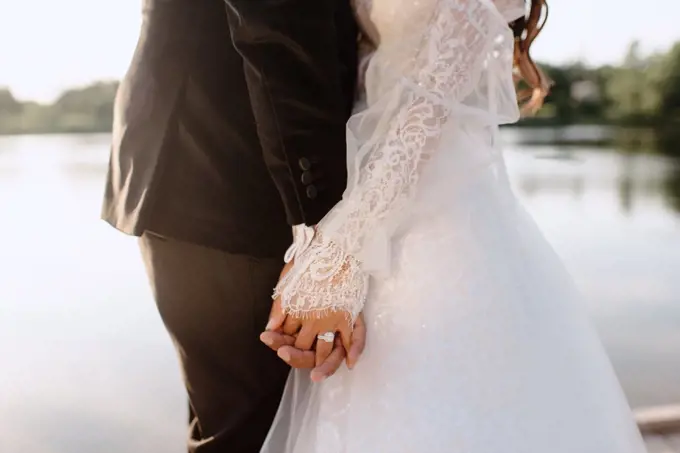 Mid section of bride and groom holding hands on lakeshore