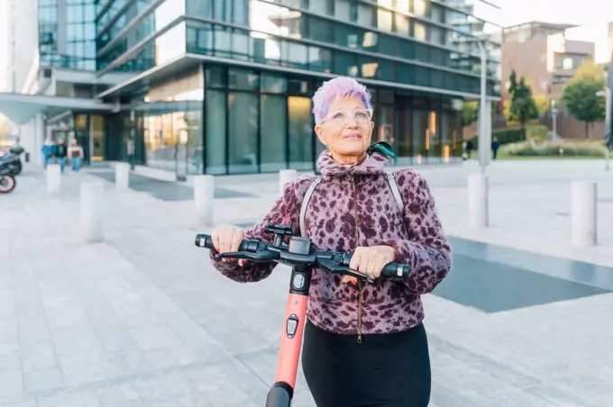 Italy, Fashionable senior woman with push scooter in city