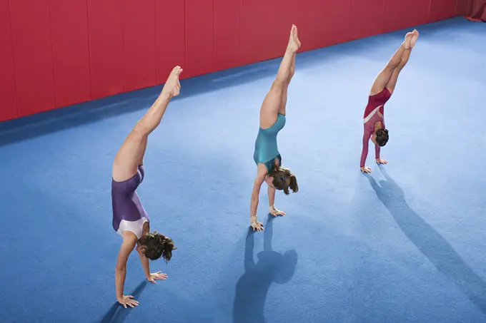 Three gymnasts perfecting their handstands in a vibrant gymnasium