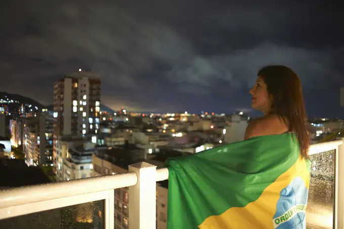 Mature woman gazing from balcony at night, Rio De Janeiro, Brazil