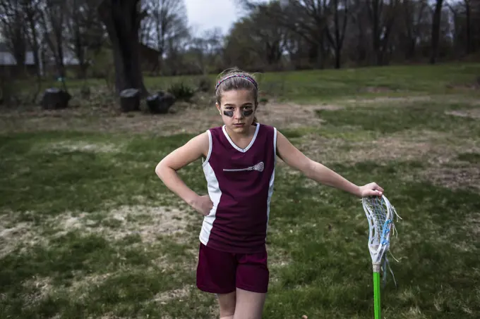 Girl wearing lacrosse uniform, leaning against lacrosse stick