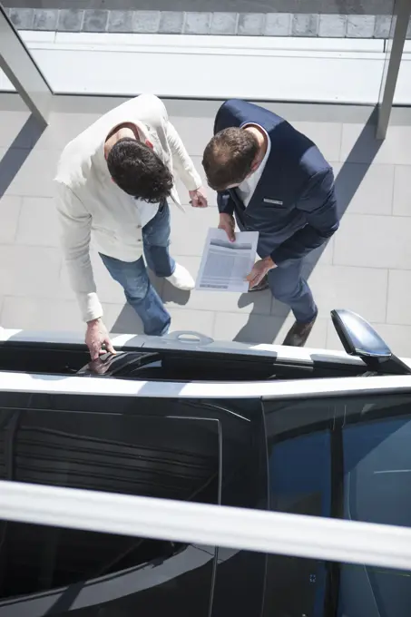 Overhead view of salesman and customer looking at new car in car dealership