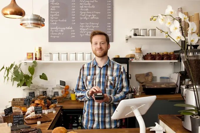 Portrait of cafe waiter with card machine behind counter