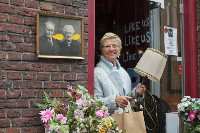 Mature female customer carrying lamp and shopping bag outside vintage shop