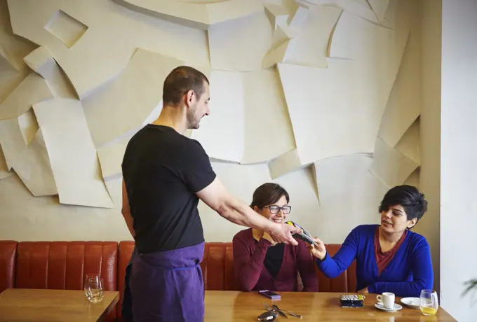 Waiter handing credit card machine to woman in restaurant