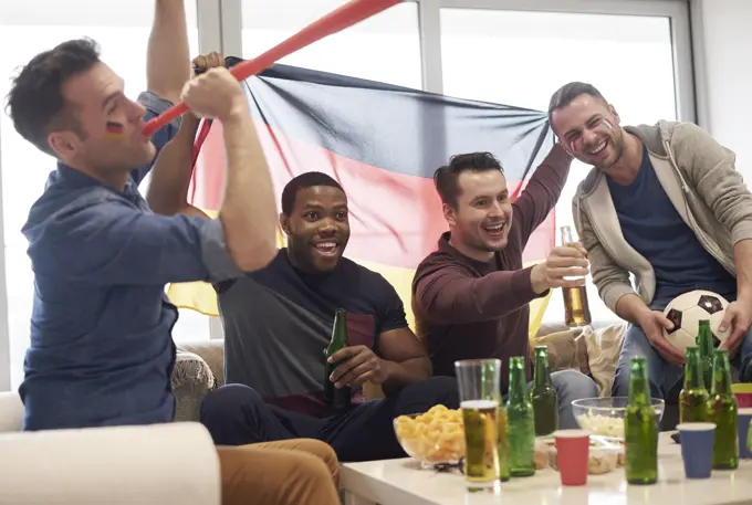 Group of men watching sporting event on television holding German flag and football, celebrating