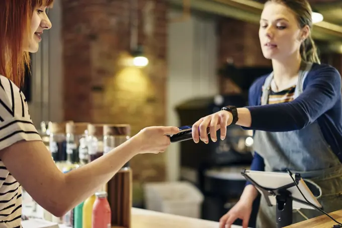 Female barista taking smartphone contactless payment from coffee shop customer