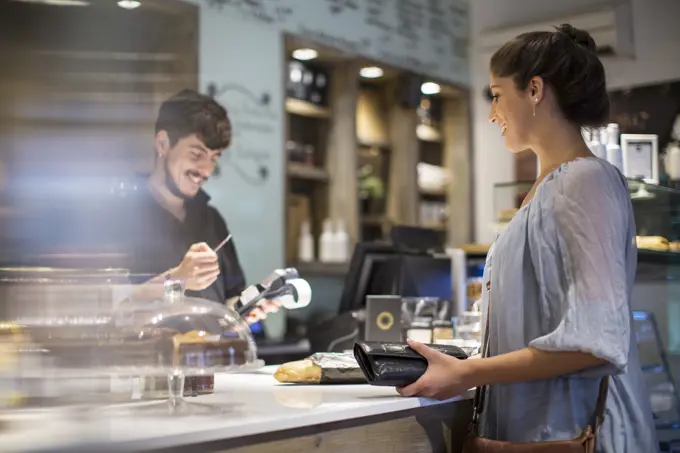 Barista calculating bill for female customer at cafe counter