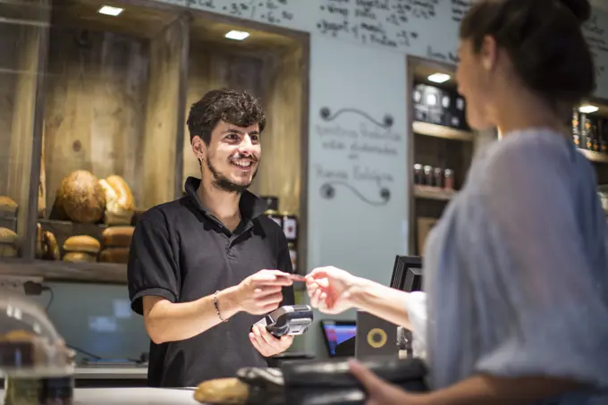 Barista handing credit card to female customer at cafe counter