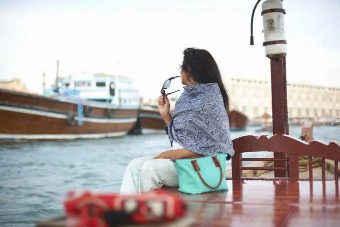 Female tourist sitting on waterfront watching boats on creek, Dubai, United Arab Emirates