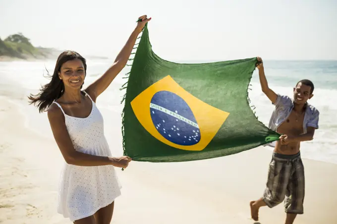 Young couple holding up Brazilian flag, Arpoador beach, Rio De Janeiro, Brazil