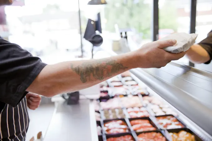 Cropped shot of butcher handing produce to customer in butchers shop