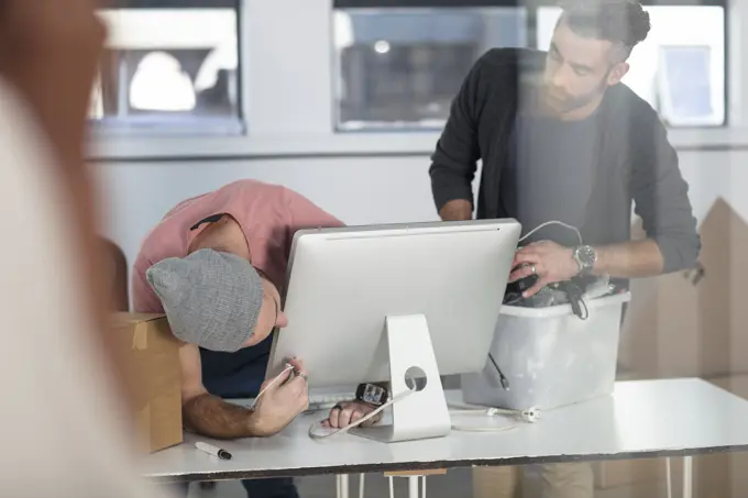 Two men working on a computer in an office setting.