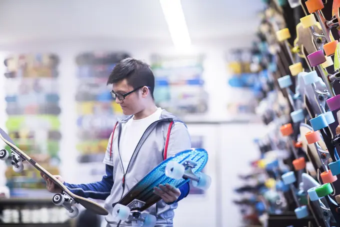 Young male skateboarder looking at skateboards in skateboard shop