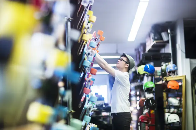 Young male skateboarder removing skateboard from wall in skateboard shop