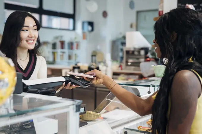 Young businesswoman making smartphone payment at cafe counter