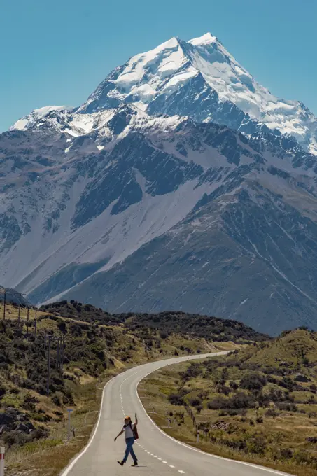 Hiker crossing road leading towards mountains, Wanaka, Taranaki, New Zealand