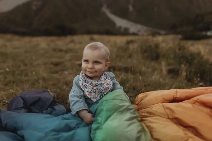 Baby sitting among jackets in wilderness, Wanaka, Taranaki, New Zealand