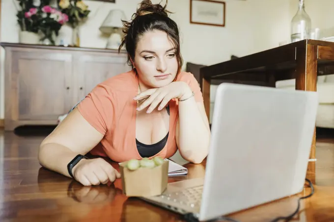 Contemplative young woman with a healthy snack taking a break from working on her laptop at home.