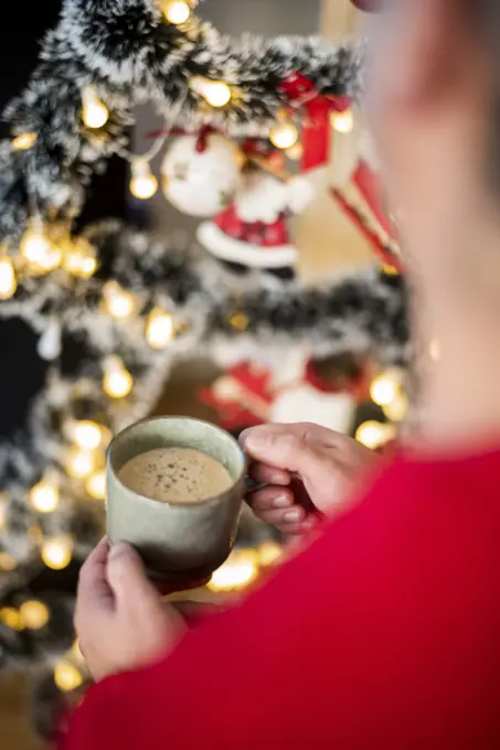 Cozy holiday moment with a warm drink in hand beside a beautifully decorated Christmas tree.