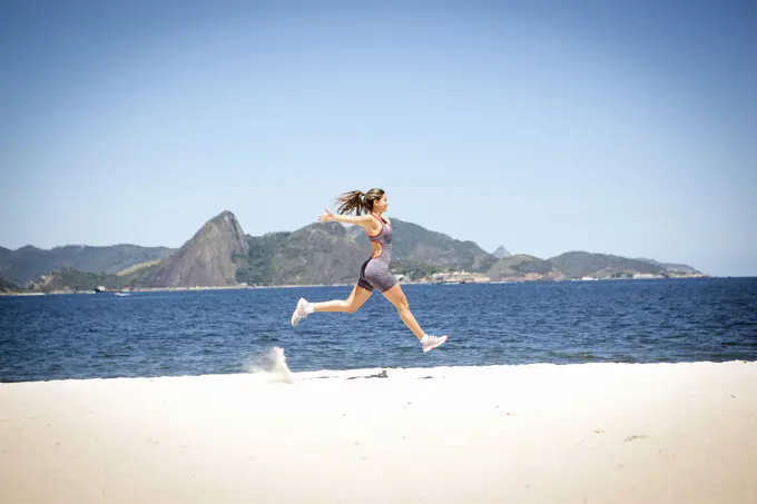 Young woman jumping on beach, Rio de Janeiro, Brazil