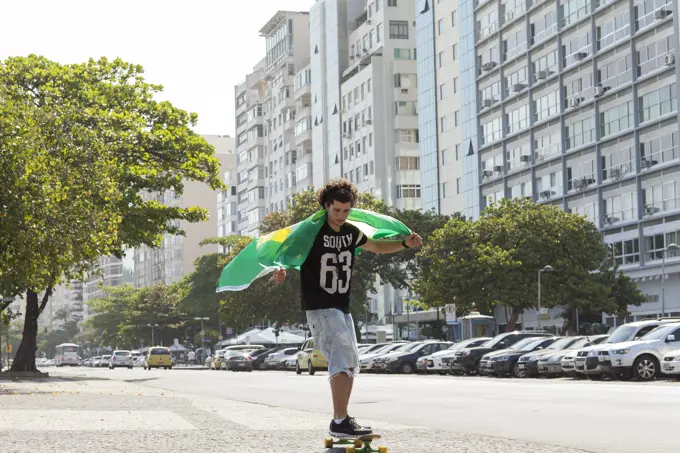 Young man skateboarding holding Brazilian flag, Copacabana, Rio De Janeiro, Brazil