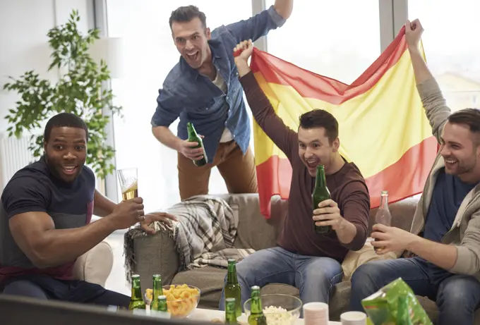 Group of men watching sporting event on television holding Spanish flag celebrating