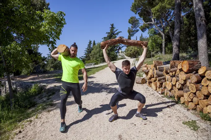 Two young men doing weightlifting training with logs in forest, Split, Dalmatia, Croatia