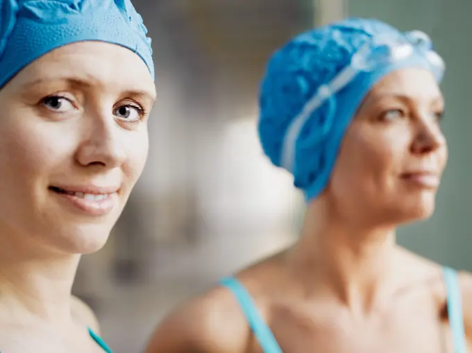 Two women wearing swimming caps and goggles smiling at the poolside