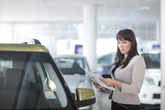 Mid adult woman checking car brochure in showroom